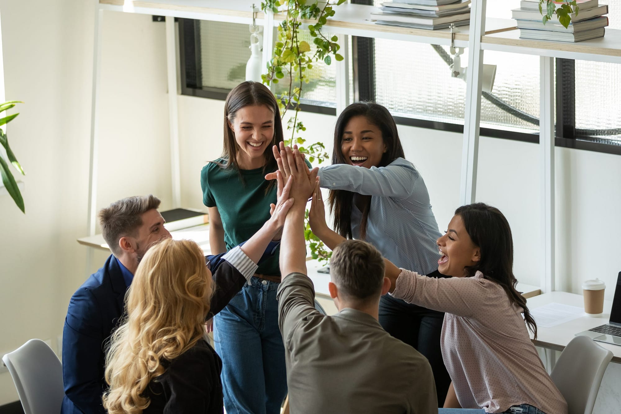 Business team colleagues of different age ethnicities join palms in high five on briefing at office feeling happy proud of mutual achievement meeting goal.